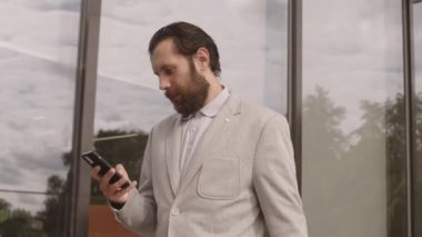 Yazın modern cam ofis binası boyunca yürürken akıllı telefonuyla konuşan ve defterindeki sayfalara bakan gri takım elbiseli beyaz sakallı iş adamının orta derecede yavaşlamış hâli.