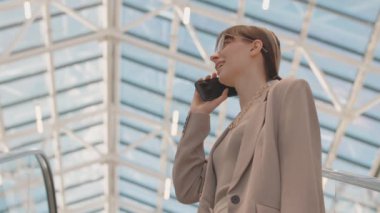 Düşük açılı, orta yaşlı, şık günlük giysili, akıllı telefonuyla konuşan, modern mağazada alışveriş yapan genç, çekici esmer kadın.