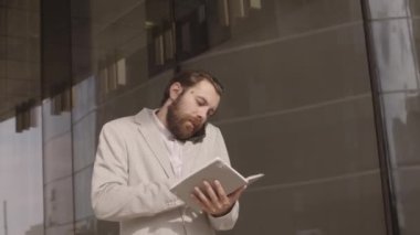 Kafkasyalı sakallı genç işadamının, şehir merkezindeki cam ofis binası boyunca yürürken cep telefonuyla ilgili notlara bakması ve başlangıç fikirlerini tartışması.