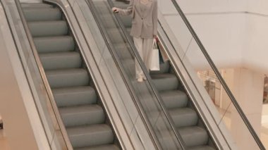 Alışveriş merkezinden alışveriş yaptıktan sonra ellerinde alışveriş torbalarıyla yürüyen merdivenden inen iki farklı kadının fotoğrafı.