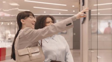 Modern alışveriş merkezinde vitrin önünde durmuş moda malzemelerini tartışırken sohbet eden iki genç kız arkadaşın yavaşlaması.