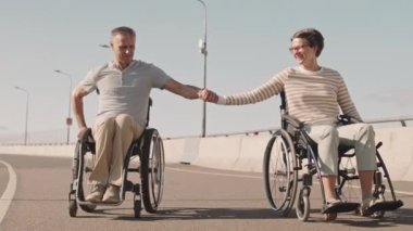 Romantik beyaz çift yazın köprü yolunda tekerlekli sandalye sürerken el ele tutuşup sohbet ediyorlar.