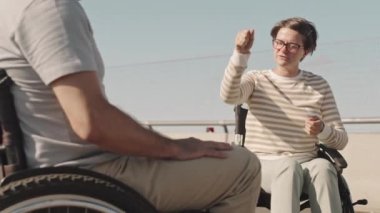 Güneşli bir günde boş köprü yolunda konuşan yetişkin beyaz tekerlekli sandalyeli çift.
