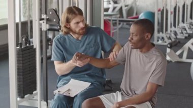 Spor salonunda fizyoterapi seansına başlamadan önce siyah erkek hastanın motor ve kol gücünü ölçen ve not alan rehabilitasyon terapistinin orta derecede yavaşlaması.