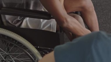 Rehabilitasyon merkezindeki fizyoterapi uzmanının yaralanmasından bahsederken bacağına ve dizine bakan tanınamayan siyah tekerlekli sandalyeli adam yavaşladı.