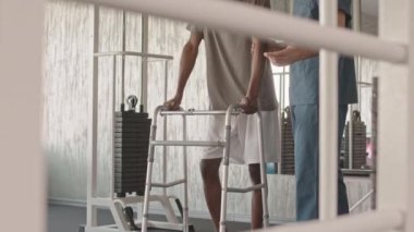 Genç Afrikalı Amerikalı adam rehabilitasyon merkezinde fizyoterapi uzmanıyla yürümeye çalışıyor.