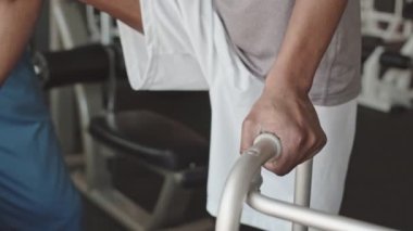 Mavi önlüklü fizyoterapist kaval kemiğini incelerken dizinden yaralanmış siyahi bir adamın aylaklara yaslanması.