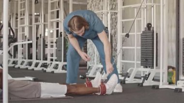 Profesyonel kinesiyoterapistin yavaş yavaş hastaların bileklerine özel ekipmanlar takması ve o yerde yatarken eklemlerini ileri geri germeye başlaması.