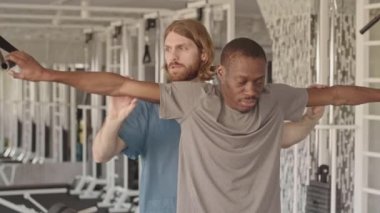 Fizyoterapistin yavaşlaması yaralanmış veya engelli bir gencin özel ekipmanlarla kol esnetme egzersizleri yapmasına yardım ediyor, modern rehabilitasyon merkezinde kişisel seans yapıyor.