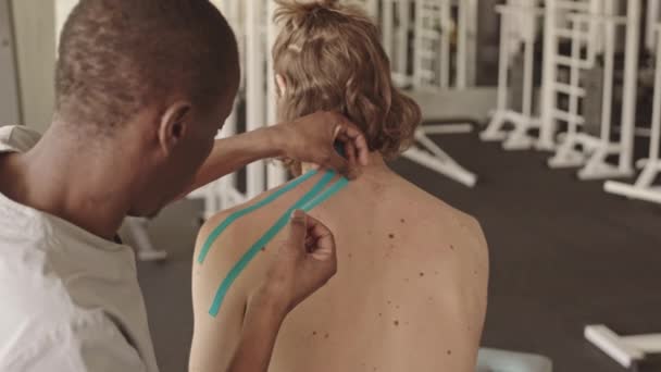 Afro Amerikaanse Fysiotherapie Specialist Bevestigen Kinesiologie Tapes Schouderblad Van Mannelijke — Stockvideo