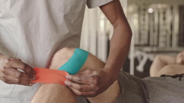 Felismerhetetlen Fizioterapeuta Kék Narancssárga Kinesio Szalagokat Erősít Férfi Beteg Térdízületére — Stock videók