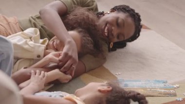 Neşe saçan Afrikalı Amerikalı kadın ve iki güzel kızı evde bulmaca çözerken yerde uzanıp eğleniyorlar.