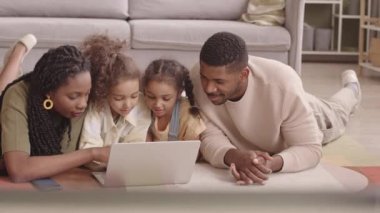 Modern Afro-Amerikan ailesinin yavaşı. Oturma odasında rahat, yumuşak bir halının üzerinde uzanmış dizüstü bilgisayar kullanıyor ve birlikte vakit geçiriyorlar.