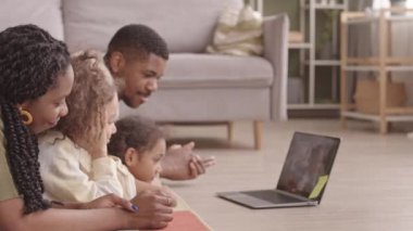Evli, Afro-Amerikan bir çift ve iki küçük kızı oturma odasında dizüstü bilgisayarda küçük bir kızla görüntülü sohbet ederken.