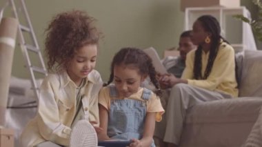 İki küçük Afrikalı Amerikalı kızın yavaş yavaş akıllı telefondan oyun oynamaları aileleri yeni geniş bir daireye taşındıktan sonra kira sözleşmesini okuyup tartışmaları.