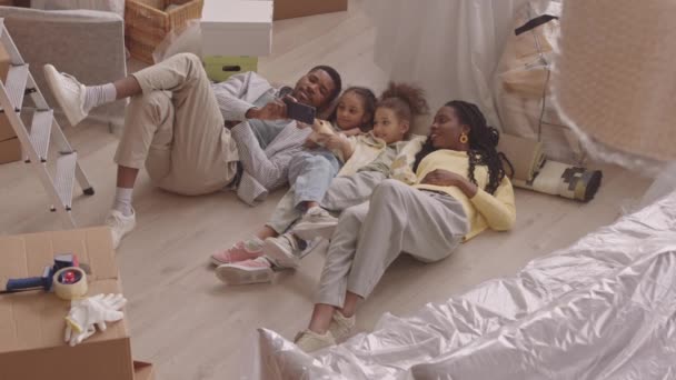 一个快乐的非洲裔美国家庭 有两个小女儿 搬进新公寓后 她们躺在纸板箱里 一边用智能手机看滑稽的视频 — 图库视频影像