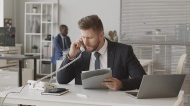 Dizüstü bilgisayarda online borsayı takip eden ve Afrikalı Amerikalı meslektaşı ile çalışırken yatırımcı veya müşteriyle telefon görüşmesi yapan takım elbiseli kendine güvenen erkek komisyoncu yavaşlıyor.