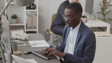 Konsantre olmuş Afro-Amerikan fon yöneticisi kablosuz klavyeyle yazarken bilgisayar üzerinde online borsa ile çalışıyor ve meslektaşı kripto para grafiği indeksini analiz ediyor.