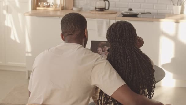 坐在简约厨房的餐桌前 与一群朋友坐在笔记本电脑上聊天的非洲裔美国夫妇的后视镜慢镜头 — 图库视频影像