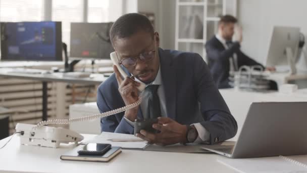 许多身穿蓝色西装的忙碌的非洲裔美国男性经纪人一边打电话与投资人交谈 一边用智能手机和笔记本电脑监控在线股市 与同事们坐在办公室里 — 图库视频影像