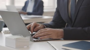 Ofis masasında dizüstü bilgisayarda yazan şık takım elbiseli tanınmayan iş adamının yakın çekimi.