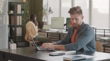 Kafkasyalı genç pazarlama uzmanı yıllık raporu okuyor, rakamları analiz ediyor ve bilgisayardan veri girişi yapıyor, modern ofiste Afrikalı Amerikalı meslektaşla telefon görüşmeleri yapıyor.