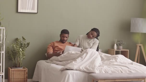 オリーブグリーンの壁と家の植物とミニマリストのエコスタイルのベッドルームの柔らかい居心地の良いベッドルームに座っている間 ラップトップ上でロマンチックな若いアフリカ系アメリカ人カップルの遅い — ストック動画
