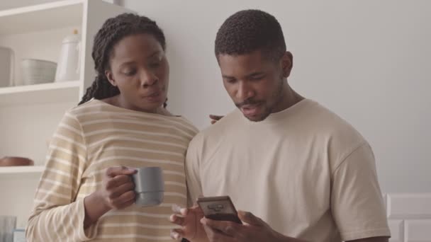 年轻的非洲裔美国人夫妇站在简约的厨房里 用智能手机点早餐 慢吞吞地等待着 — 图库视频影像