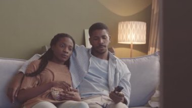 Genç Afrikalı Amerikalı çiftin TV izlediği ve akşamları kanepede oturup patlamış mısır yediği bir ortam. Erkek kız arkadaşını kucaklıyor.