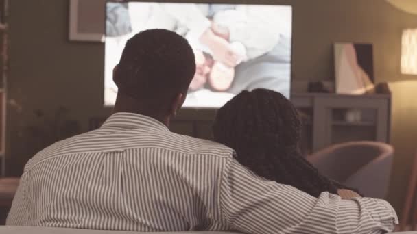周末晚上 一对年轻的非洲裔美国夫妇坐在客厅的沙发上 观看着电视上关于父亲和幼儿的温馨电影 — 图库视频影像