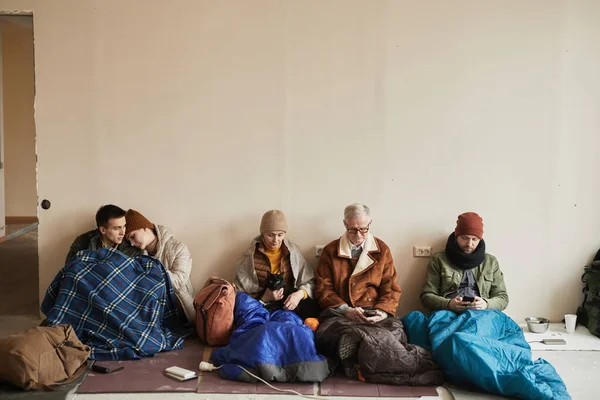 Minimal front view at diverse group of refugees hiding in shelter together during war or crisis, copy space