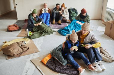 Battaniyelerle kaplı bir sığınakta saklanırken yemek yiyen bir grup Kafkasyalı mülteciye yüksek açılı bakış açısı