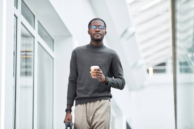 Sabah işe başlarken ofis binasında kameraya doğru yürüyen genç siyahi işadamının minimal portresi, boşluğu kopyala