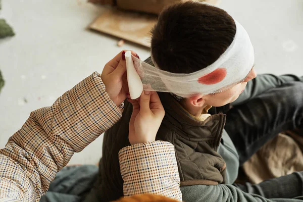 大角度护士长包扎头部受伤平民在难民庇护所 复制空间 — 图库照片