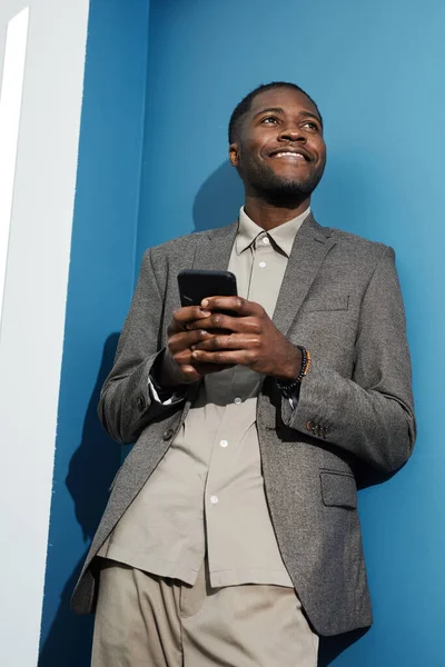 Živý Portrét Mladého Černého Podnikatele Držícího Telefon Modré Stěny Dívajícího — Stock fotografie
