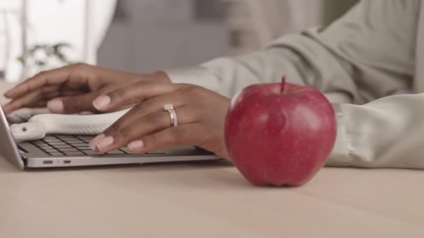 在笔记本电脑键盘和写字台上爬行的白色宠物蛇的慢镜头特写 把自己包裹在红苹果周围 而在笔记本电脑上打字的黑人妇女则无法辨认 — 图库视频影像