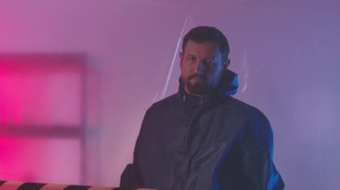 Beyaz erkek bilim adamının koruyucu tulumlar içindeki orta yavaş portresi polietilen boyunca yürüyor ve elleri katlı kameraya poz veriyor, gizli bir laboratuvarda çalışıyor.