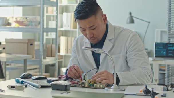 Medium Slowmo Focused Male Asian Engineer White Coat Soldering Motherboard — Stock Video