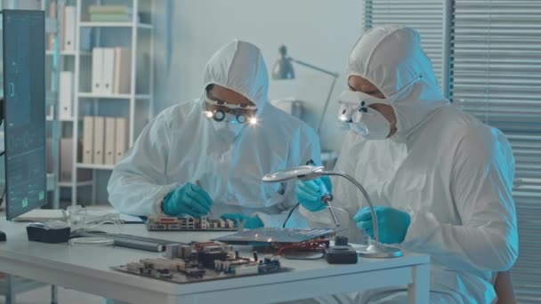 两名穿着工作服的男性技师坐在实验室的办公桌前 通过放大镜观察母板焊接部分的中等速度 — 图库视频影像