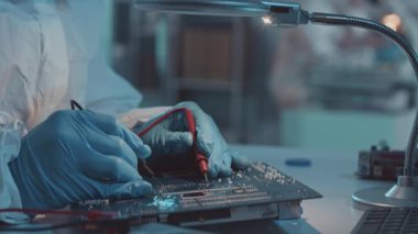 Eldivenli ve koruyucu tulumlu tanınmayan teknisyenlerin modern laboratuardaki lehimleme devre kartlarını yavaş yavaş kapatması.