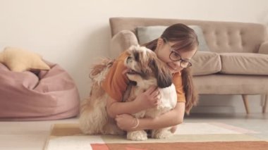 12 yaşında, Kafkasyalı bir kız, oturma odasında şirin Shih Tzu köpeğine sarılıyor.