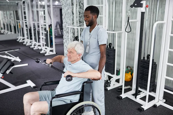 stock image Portrait of African American rehabilitation therapist assisting senior man using wheelchair in gym, copy space