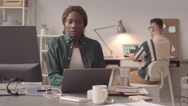 中等速度的年轻黑人女性在办公室开发软件 而她的男性同事则在笔记本电脑上输入背景信息 — 图库视频影像