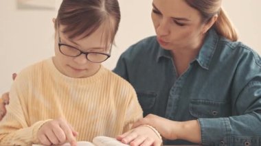 Bel yukarı, aşağı sendromlu beyaz bir kız ve sevgili annesi oturma odasında oturmuş kitap okuyor.
