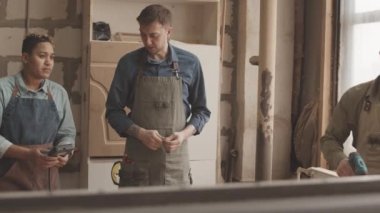 Çeşitli ahşap işçileri atölyede ahşap kalasın başında projeye başlıyorlar. Tahtada delik açmak için matkap kullanan adam.