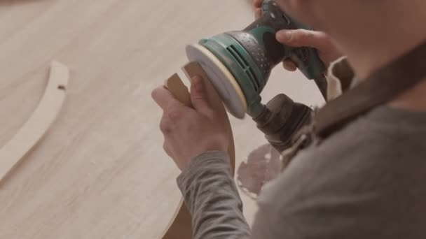 角度研削盤を使用して大工の肩のショットの上に木の彫刻作品を研磨しながら ワークショップで家具を作る — ストック動画