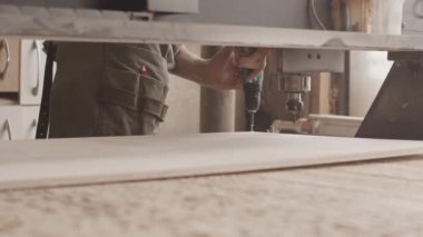 Tanınmayan erkek marangoz, sondaj gücüyle ahşap tahtada delik açıyor, CNC makinesiyle ahşap atölyesinde çalışıyor.