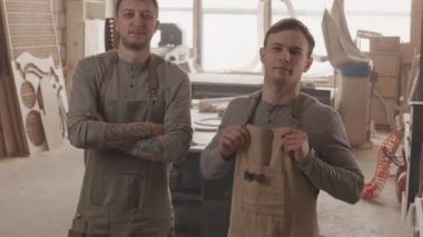 Ahşap fabrikasında kameraya poz veren önlüklü iki genç marangoz portresi.