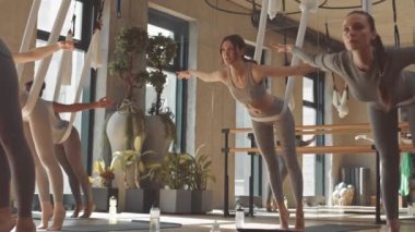 Aktif giyimli bir grup genç kadın geniş ve parlak stüdyoda panoramik pencereli hava yogası yapıyorlar.