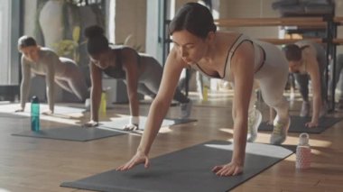 Stüdyodaki spor eğitimi sırasında paspasların üzerinde duran kadın fitness eğitmeni ve bir grup çok ırklı genç kadın.